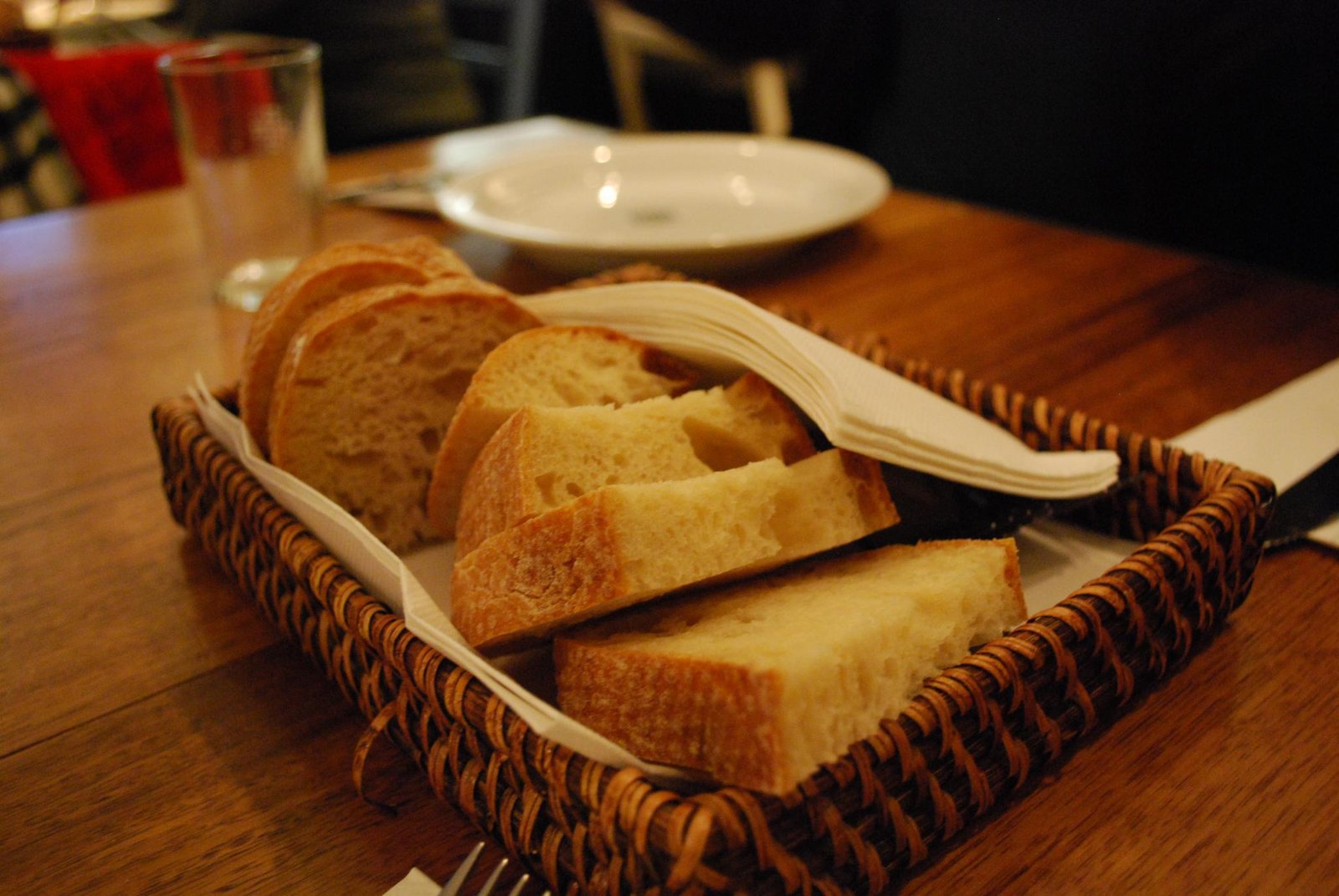 Basket of sliced bread on a wooden table with a glass and plate in the background.